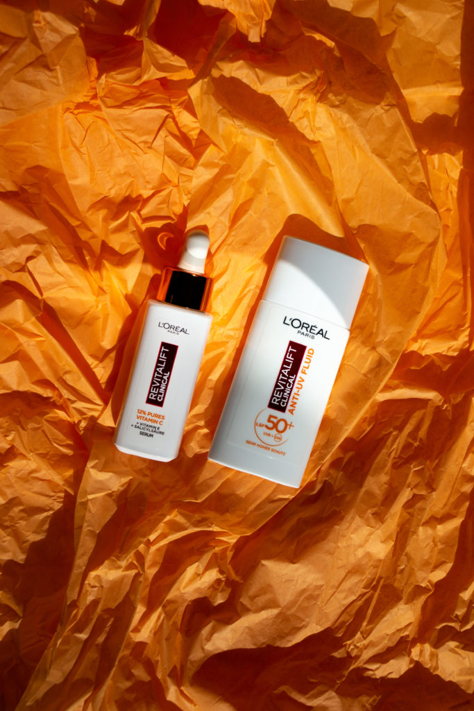L'Oréal Revitalift Clinical Serum und Sonnencreme auf einem orangen Hintergrund drapiert und mit Sonnenlicht beleuchtet