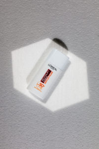 L'Oréal Revitalift Clinical Sonnencreme auf einem weissen Hintergrund drapiert und mit Sonnenlicht beleuchtet