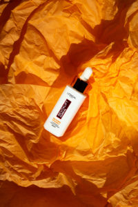 L'Oréal Revitalift Clinical Serum auf einem orangen Hintergrund drapiert und mit Sonnenlicht beleuchtet