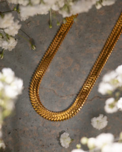 Halskette auf einem Beton Boden mit weissen Blumen inszeniert.
